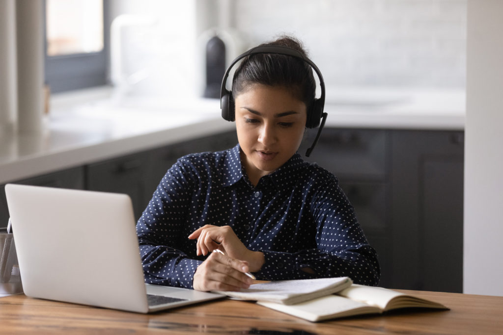 Female sitting by laptop wearing headphones getting education online
